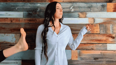 A Woman Is Standing In Front Of A Wooden Wall GIF