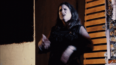 A Woman Is Standing In Front Of A Wooden Wall GIF