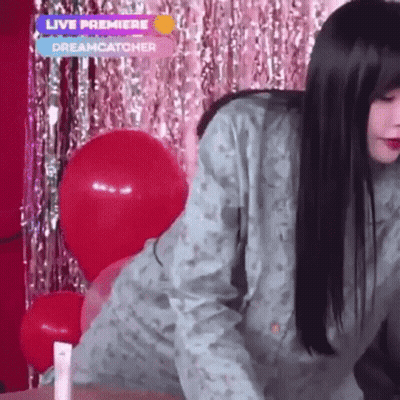 A Woman Is Standing In Front Of Balloons And A Live Premiere Sign GIF