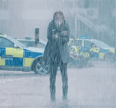 A Woman Is Standing In The Rain In Front Of A Police Car Holding A Cell Phone . GIF