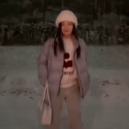 A Woman Is Standing In The Snow Wearing A Hat And A Sweater . GIF
