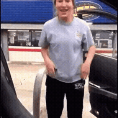 A Woman Is Standing Next To A Car At A Gas Station And Smiling . GIF