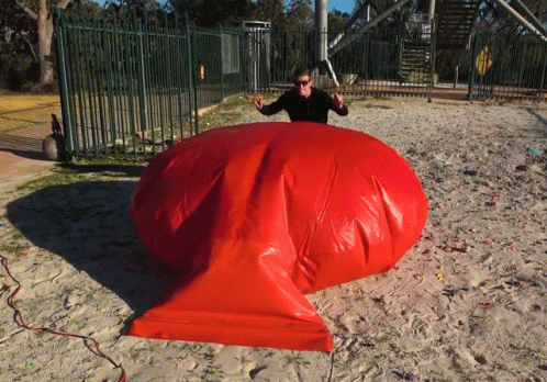 A Woman Is Standing Next To A Large Red Inflatable Object GIF