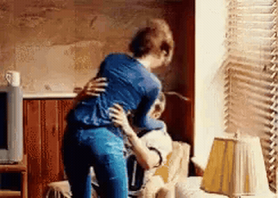 A Woman Is Standing Next To A Man In A Living Room Hugging Him . GIF