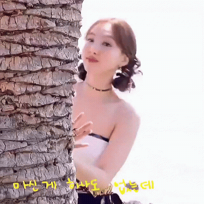 A Woman Is Standing Next To A Palm Tree Looking At The Camera . GIF