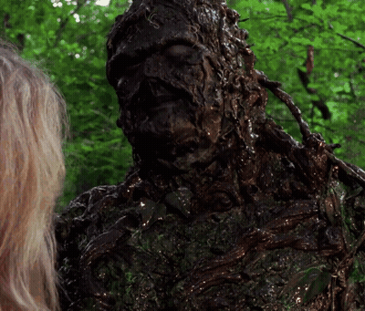 A Woman Is Standing Next To A Statue Of A Monster Covered In Mud GIF