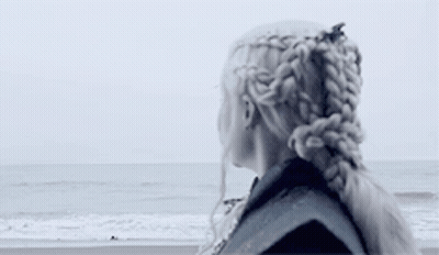 A Woman Is Standing On A Beach Looking At The Ocean . GIF