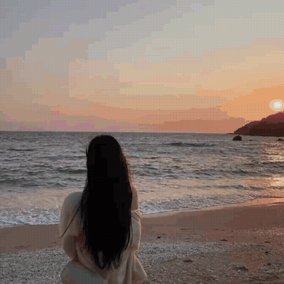 A Woman Is Standing On A Beach Looking At The Ocean GIF