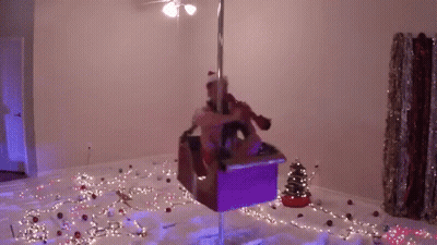 A Woman Is Standing On A Pole In A Room With Christmas Lights . GIF