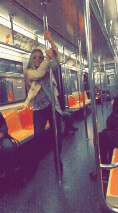 A Woman Is Standing On A Pole In A Subway Car GIF