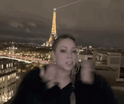 A Woman Is Standing On A Rooftop In Front Of The Eiffel Tower At Night . GIF