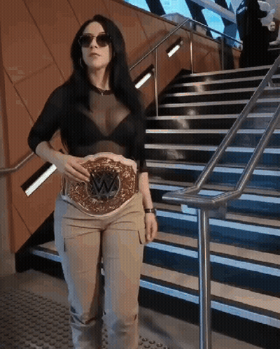 A Woman Is Standing On A Set Of Stairs Holding A Wrestling Belt On Her Waist . GIF