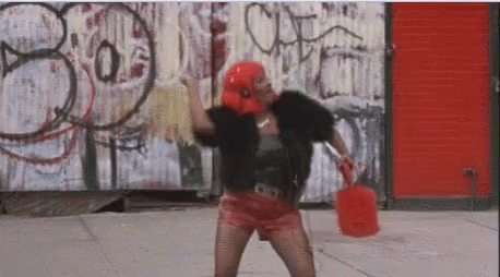 A Woman Is Standing On A Sidewalk Holding A Red Bucket And A Mop . GIF