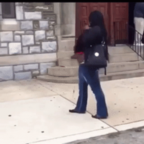 A Woman Is Standing On A Sidewalk In Front Of A Building GIF