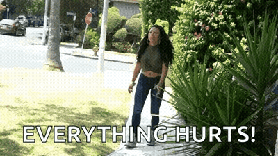 A Woman Is Standing On A Sidewalk With The Words `` Everything Hurts '' Written On The Ground . GIF