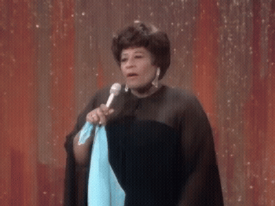 A Woman Is Standing On A Stage Holding A Microphone And A Blue Cloth . GIF