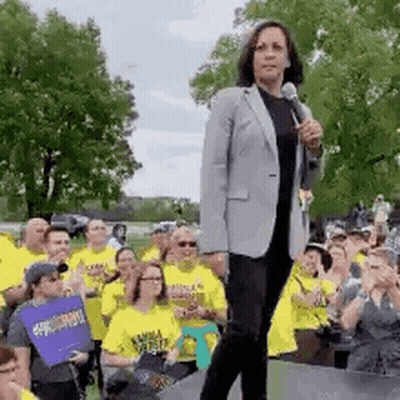 A Woman Is Standing On A Stage Holding A Microphone In Front Of A Crowd Of People Wearing Yellow Shirts . GIF