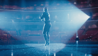A Woman Is Standing On A Stage In Front Of An Empty Auditorium GIF