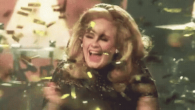 A Woman Is Standing On A Stage Surrounded By Confetti And Laughing . GIF