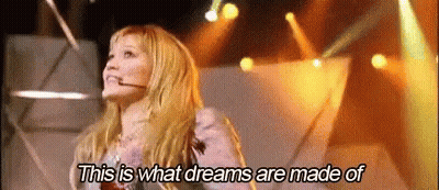 A Woman Is Standing On A Stage With A Microphone In Her Mouth . GIF