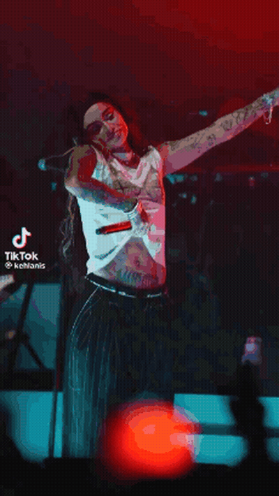 A Woman Is Standing On A Stage With Her Arms Outstretched While Singing Into A Microphone . GIF