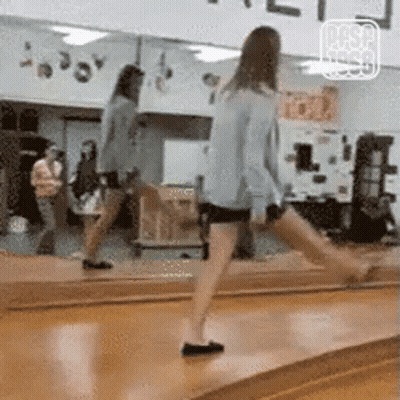 A Woman Is Standing On A Wooden Floor In Front Of A Large Mirror . GIF