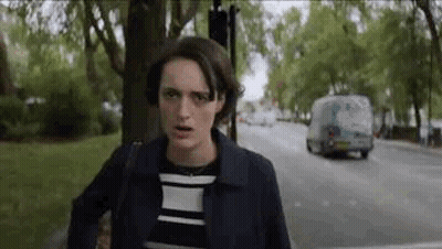 A Woman Is Standing On The Side Of A Street Looking At The Camera . GIF
