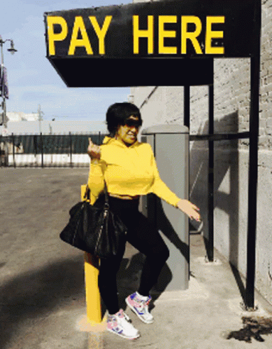 A Woman Is Standing Under A Sign That Says Pay Here GIF