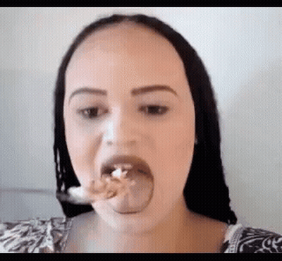 A Woman Is Sticking Her Tongue Out While Eating A Piece Of Food With A Spoon . GIF
