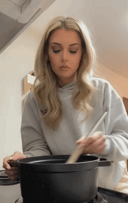 A Woman Is Stirring A Pot Of Food With A Wooden Spoon . GIF