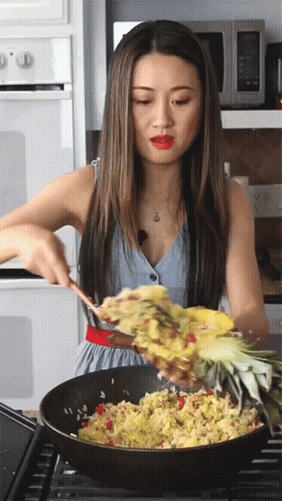 A Woman Is Stirring Food In A Pan With A Pineapple GIF