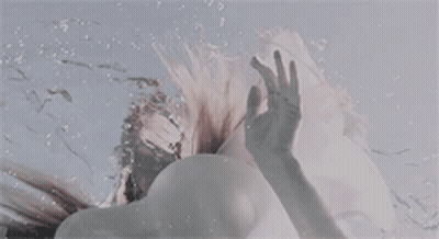 A Woman Is Swimming Underwater And Reaching Out Towards The Sky . GIF