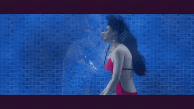 A Woman Is Swimming Underwater In A Pool And Looking At Her Reflection . GIF