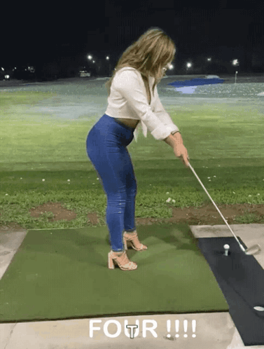 A Woman Is Swinging A Golf Club On A Green Mat With Four Written On The Ground GIF