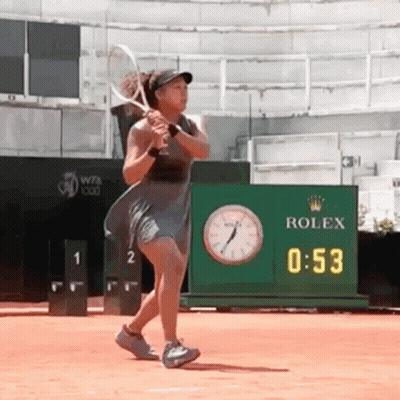 A Woman Is Swinging A Tennis Racquet In Front Of A Rolex Clock GIF