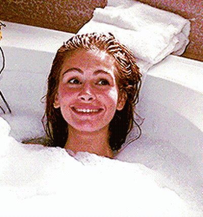 A Woman Is Taking A Bath In A Bathtub And Smiling GIF