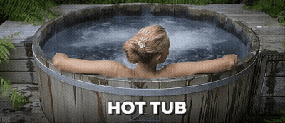 A Woman Is Taking A Bath In A Wooden Tub With The Words Hot Tub Below Her GIF