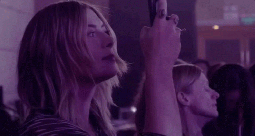 A Woman Is Taking A Picture Of A Crowd Of People At A Concert . GIF