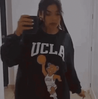 A Woman Is Taking A Picture Of Herself In A Mirror While Wearing A Ucla Sweatshirt . GIF