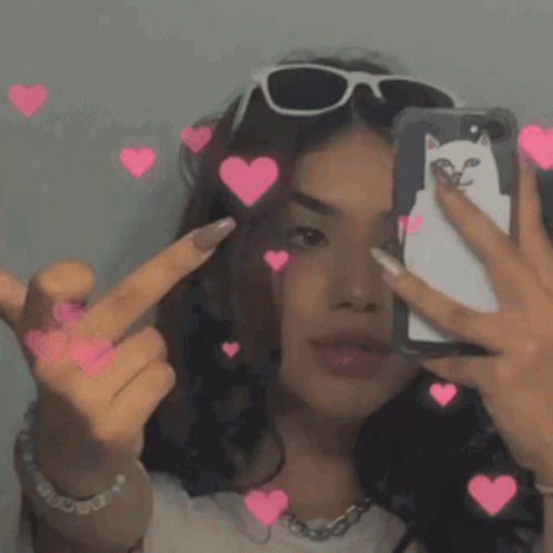 A Woman Is Taking A Picture Of Herself In A Mirror With Hearts Coming Out Of Her Hair . GIF