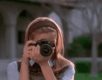 A Woman Is Taking A Picture With A Camera And Smiling . GIF