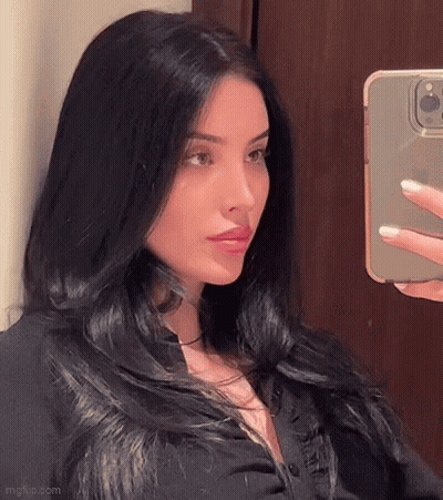 A Woman Is Taking A Selfie In Front Of A Mirror With Her Cell Phone . GIF
