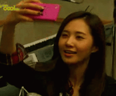 A Woman Is Taking A Selfie With A Pink Cell Phone GIF