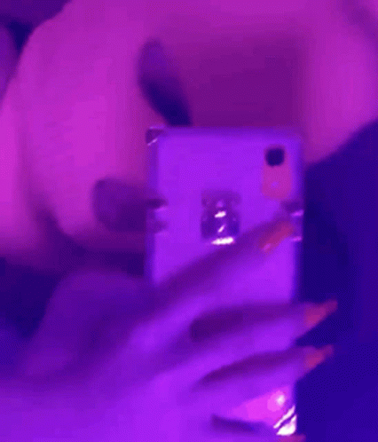 A Woman Is Taking A Selfie With Her Cell Phone In A Purple Light . GIF