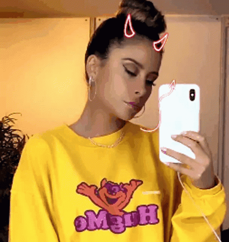 A Woman Is Taking A Selfie With Her Phone While Wearing A Yellow Shirt That Says Mr. Men GIF