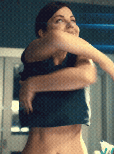 A Woman Is Taking Off Her Shirt And Looking At The Camera GIF