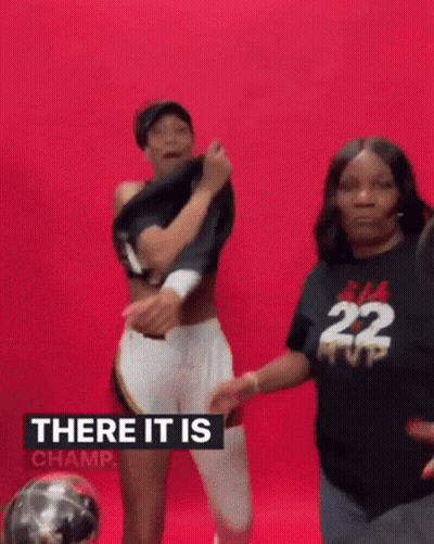A Woman Is Taking Off Her Shirt While Standing Next To Another Woman In A Black Shirt With The Number 22 On It . GIF