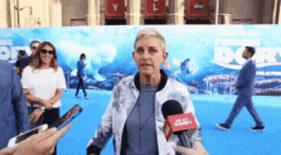 A Woman Is Talking Into A Microphone While Standing In Front Of A Sign That Says Finding Dory . GIF