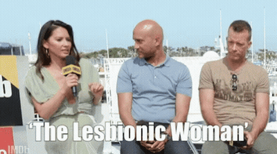 A Woman Is Talking Into A Microphone While Two Men Sit Behind Her With The Words " The Lesbian Woman " Written Below The GIF