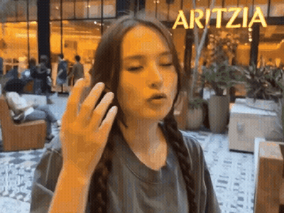 A Woman Is Talking On A Cell Phone In Front Of A Sign That Says Aritzea . GIF